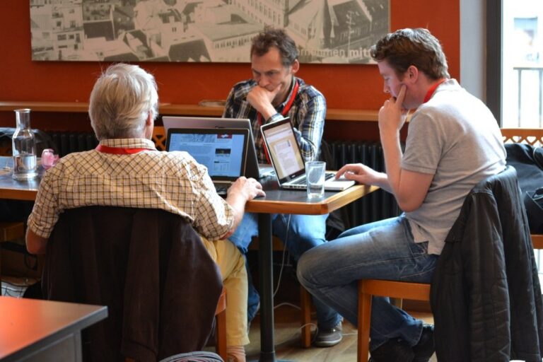 Teams at laptops at several tables