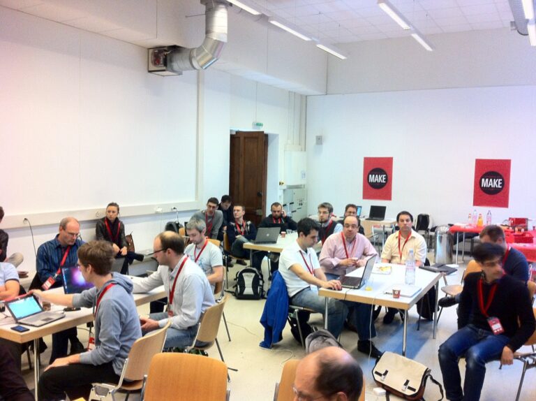 Voller Saal mit Teilnehmenden an Laptops, MAKE-Plakate an der Wand