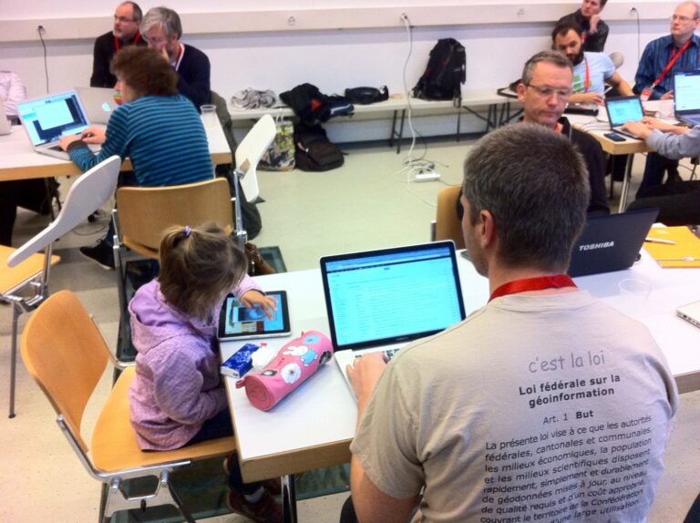 Teilnehmende an Laptops, vorne ein Mann im T-Shirt mit dem Text des Geoinformationsgesetzes